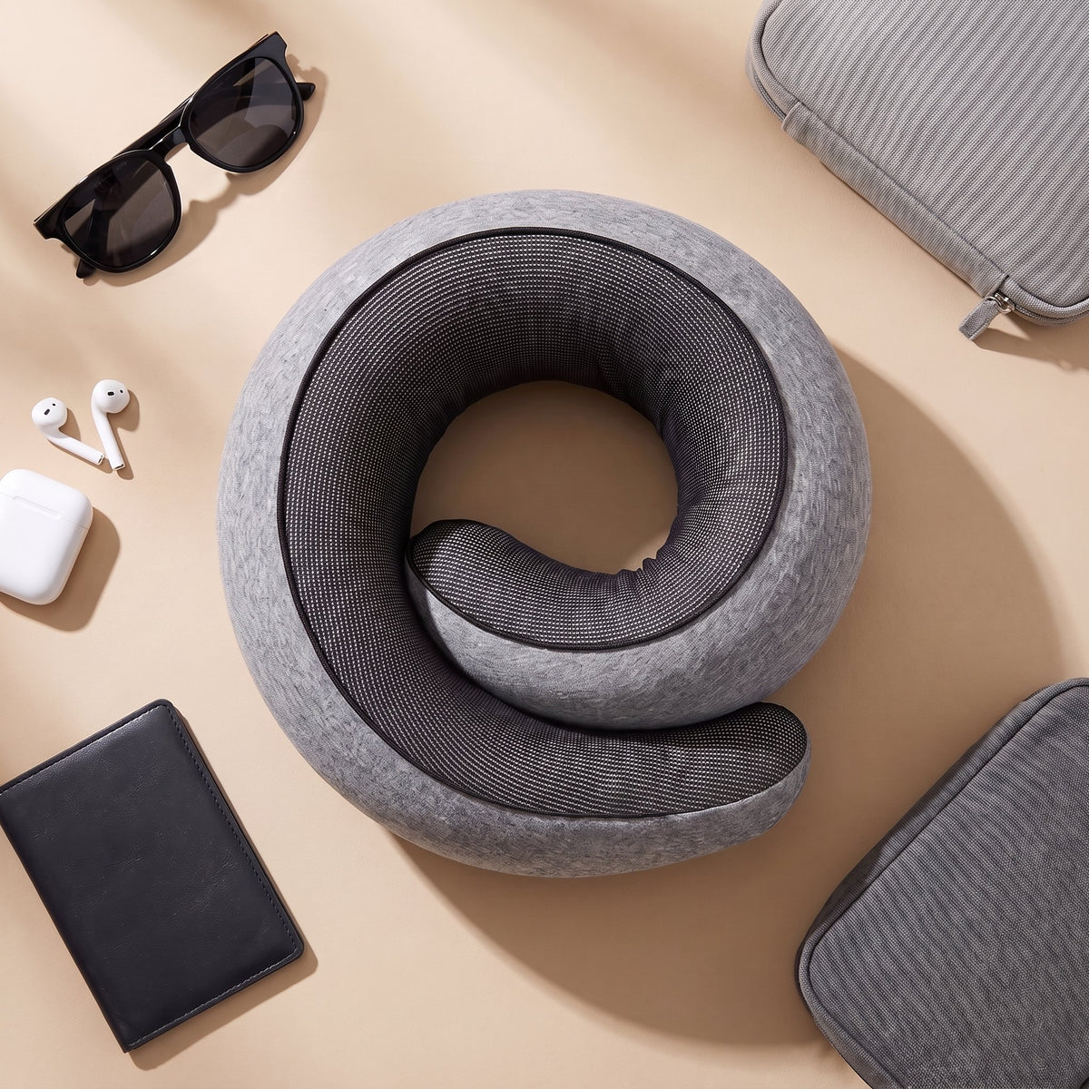 The travel pillow laid flat with sunglasses, earphones, a passport wallet and travel pouches